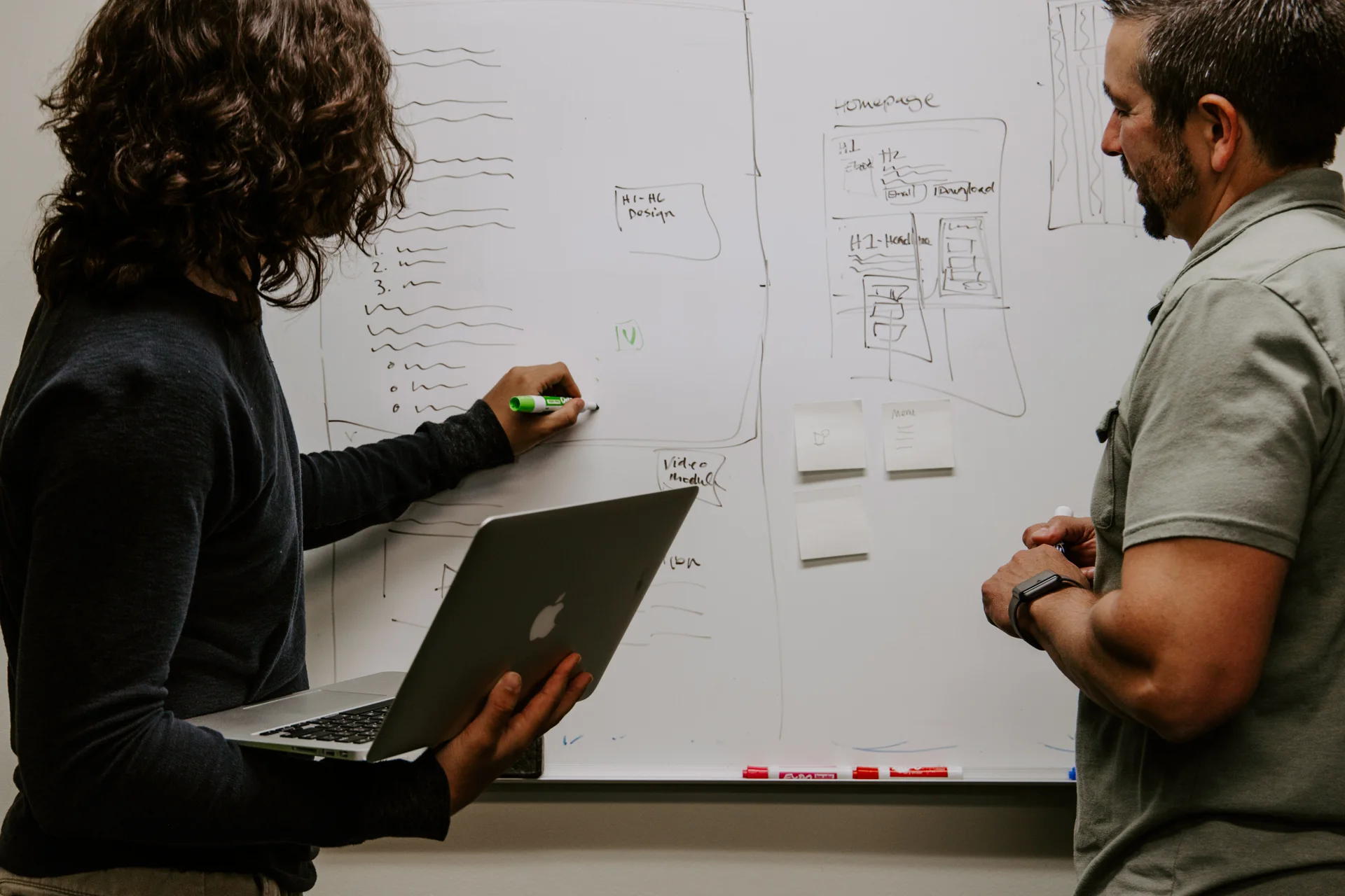 Two people sketching interface flows on a whiteboard.